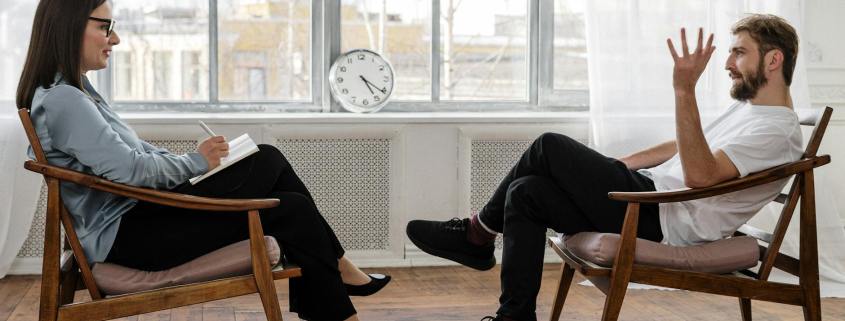 person in black pants and black shoes sitting on brown wooden chair